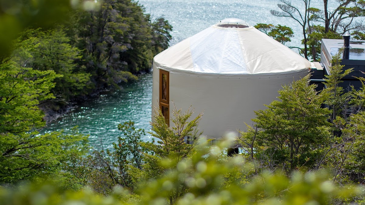 White yurt with wooden door sits on hillside overlooking turquoise river and surrounding forest at Patagonia Camp.