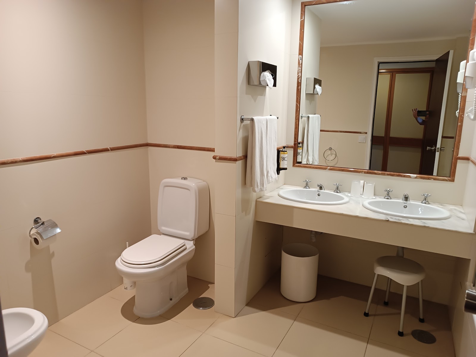 Bathroom with two white round sinks, wooden-framed mirror, toilet, and tan tile walls with wood trim at Pestana Blue Alvor Beach.