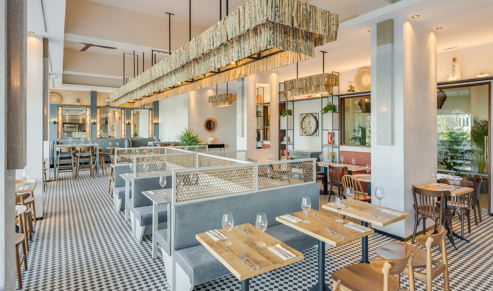 Modern restaurant dining room with wooden tables, gray banquette seating, woven pendant lights, and checkered flooring at Pestana Blue Alvor Beach.