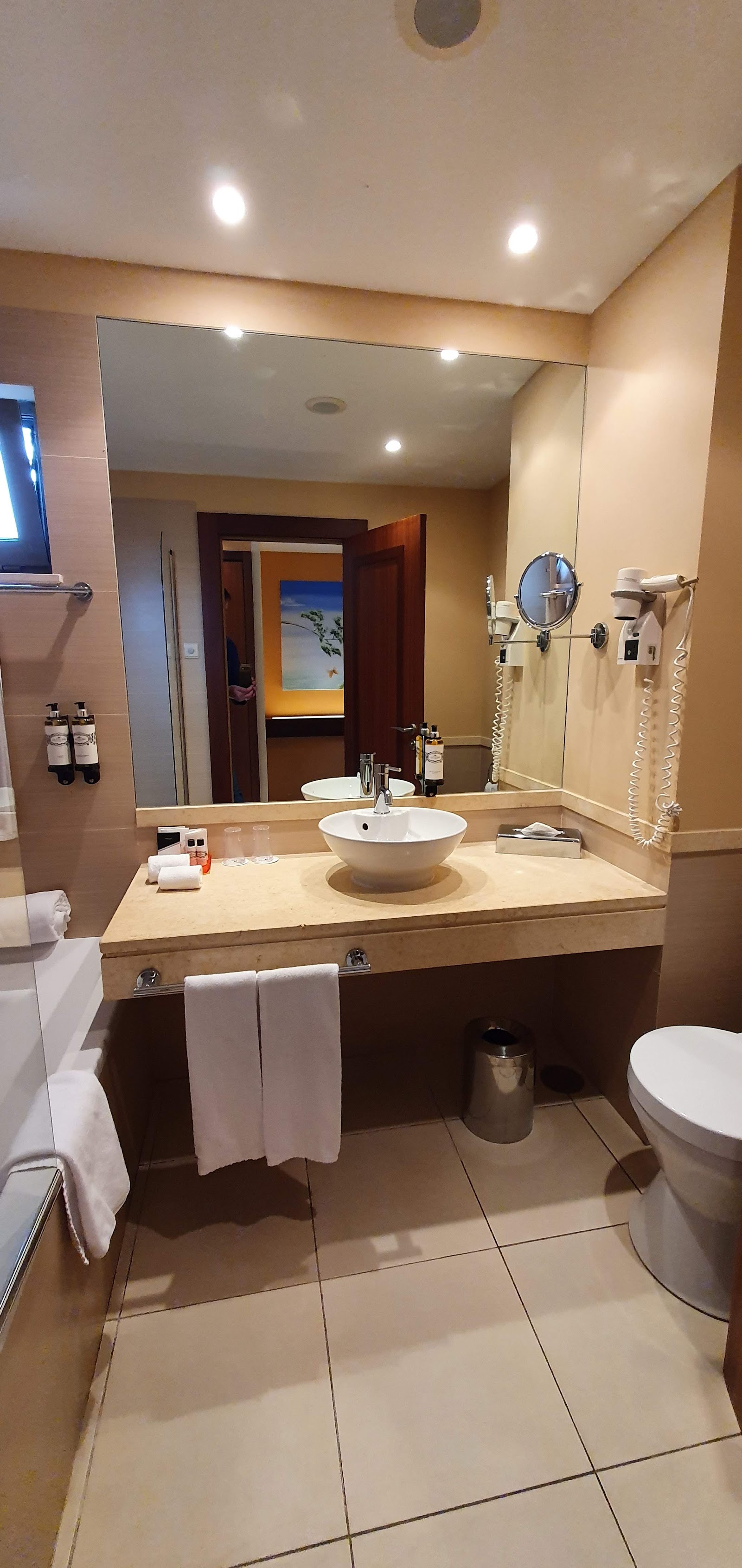 Resort bathroom with round white vessel sink, large mirror, beige countertop, and warm lighting.