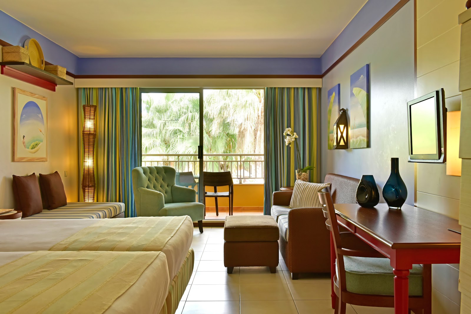 Hotel room with queen bed, blue accent ceiling, red lamps, striped seating areas, and work desk at Pestana Porto Santo All Inclusive.