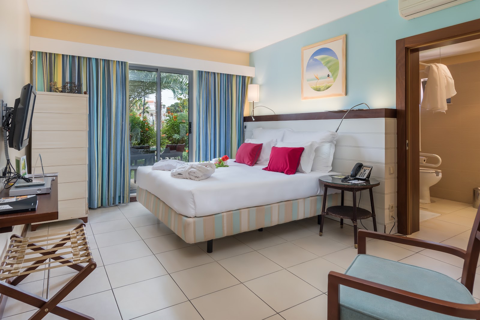 Covered wooden deck with mint and coral chairs at tables overlooking mangroves and ocean at Pestana Porto Santo All Inclusive.
