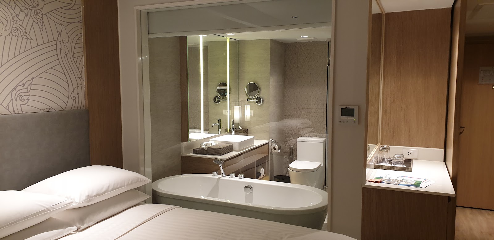 Modern resort bathroom with soaking tub, dual vanity, and walk-in shower behind glass partition, adjoining bedroom visible on left.