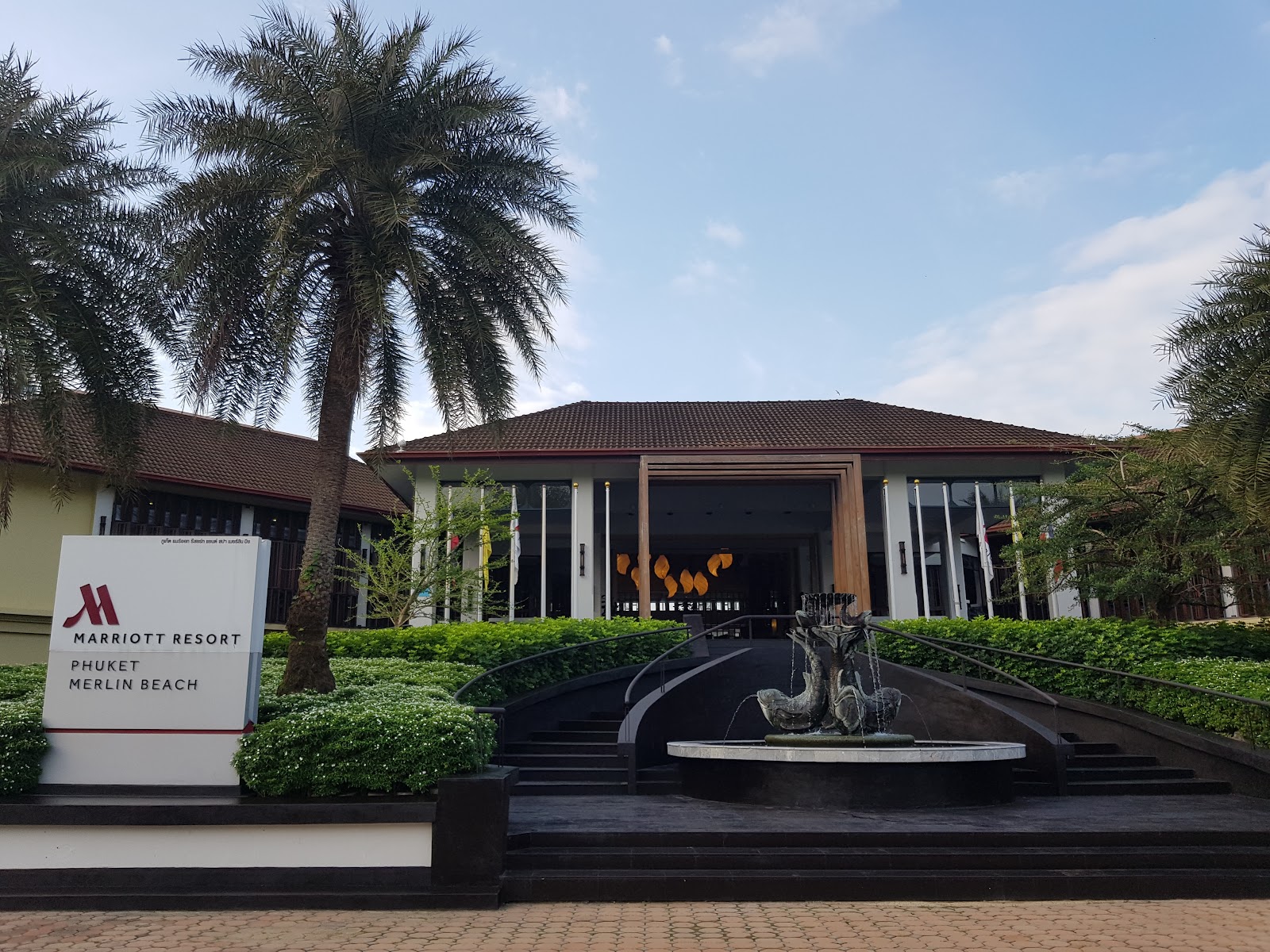 Marriott Resort Phuket Merlin Beach entrance with palm trees, dragon statue fountain, and modern low-rise building with dark roof.