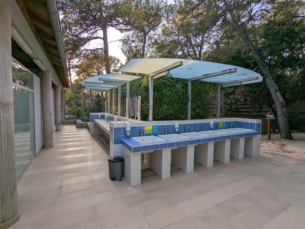 Outdoor bathroom facility with blue-tiled sinks under a white pergola, surrounded by tall trees at Pine Beach Pakoštane Adriatic Eco Resort.