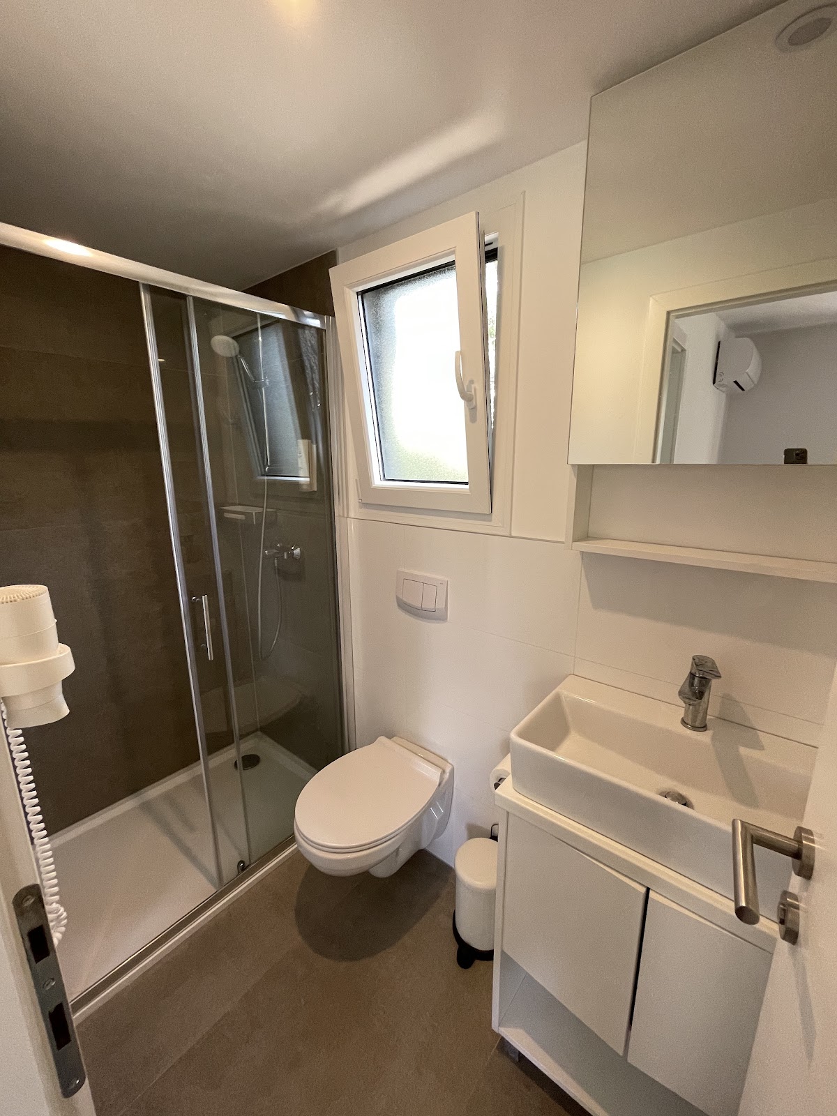 Bright modern bathroom with glass-enclosed shower, white sink vanity, toilet, and mirror at Pine Beach Pakoštane Adriatic Eco Resort.