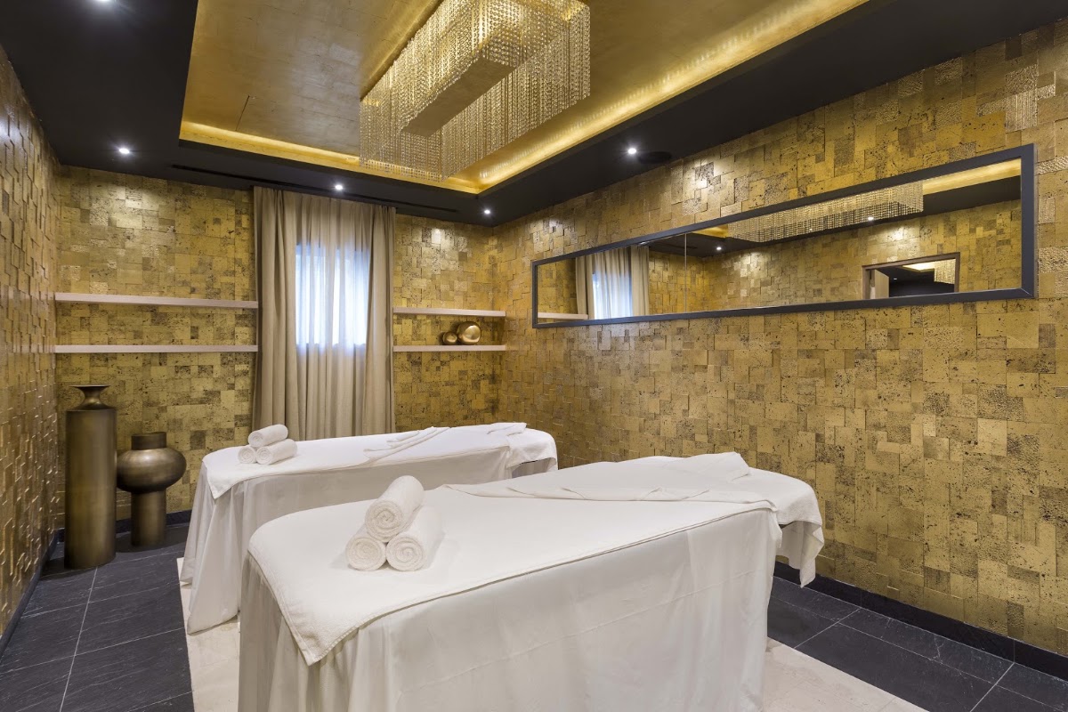 Spa treatment room with two massage tables draped in white linens, gold mosaic tile walls, and ambient lighting at Pine Cliffs Resort.