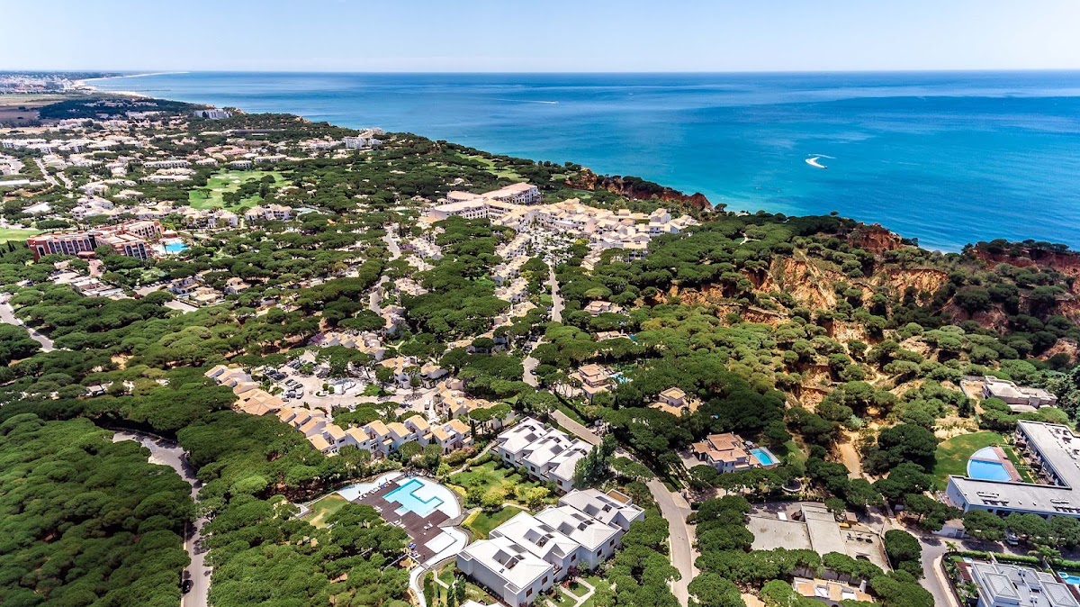 Aerial view of Pine Cliffs Resort nestled in greenery above turquoise ocean, with sandy cliffs and coastal landscape stretching along the Algarve shoreline.