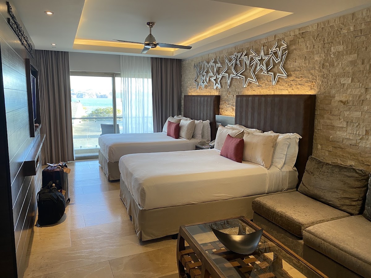 Resort room with two queen beds, stone accent wall, ceiling fan, and ocean view from balcony doors at Planet Hollywood Costa Rica by Royalton.