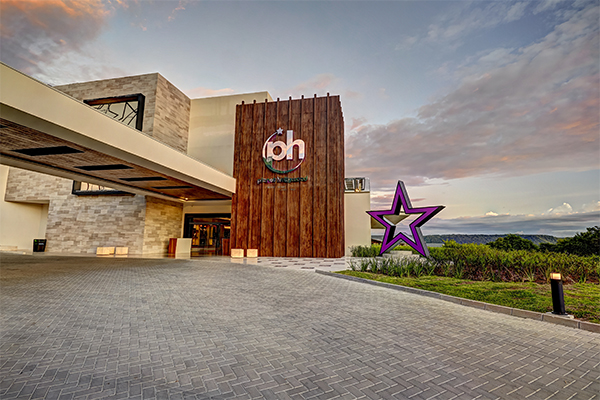 Exterior of Planet Hollywood Costa Rica resort at dusk with wooden tower featuring logo and purple star sculpture beside entrance.