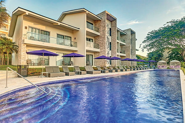 Planet Hollywood Costa Rica by Royalton features a modern multi-story building with stone and stucco exterior beside a sparkling blue pool under purple umbrellas and lounge chairs.
