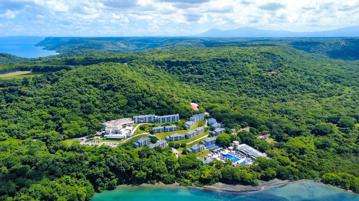 Planet Hollywood Costa Rica by Royalton nestled in dense jungle with turquoise bay and distant coastline visible below.