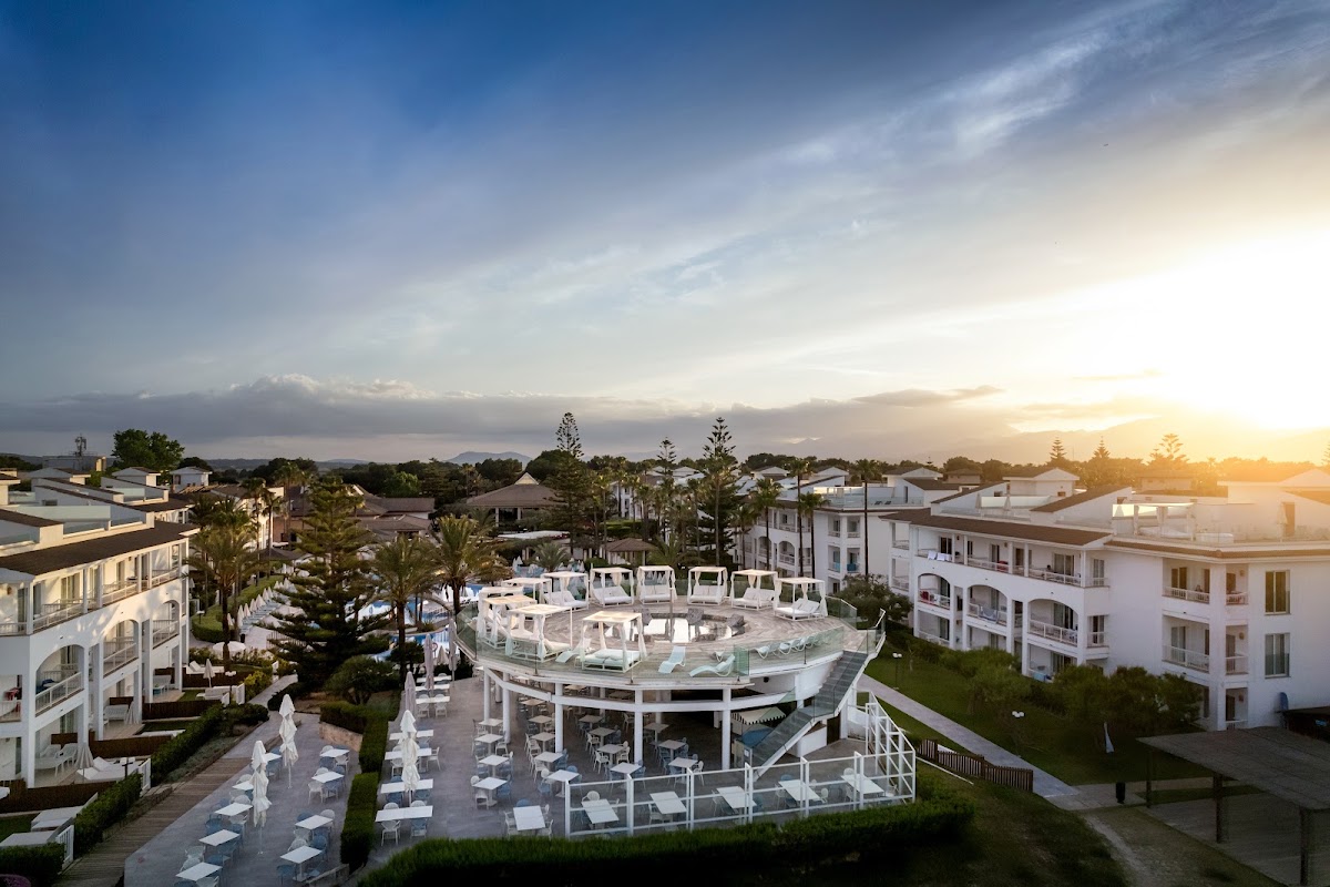 Aerial view of Playa Garden Selection Hotel & Spa at sunset with white buildings, central pool area, lounge chairs, and palm trees surrounding the resort.