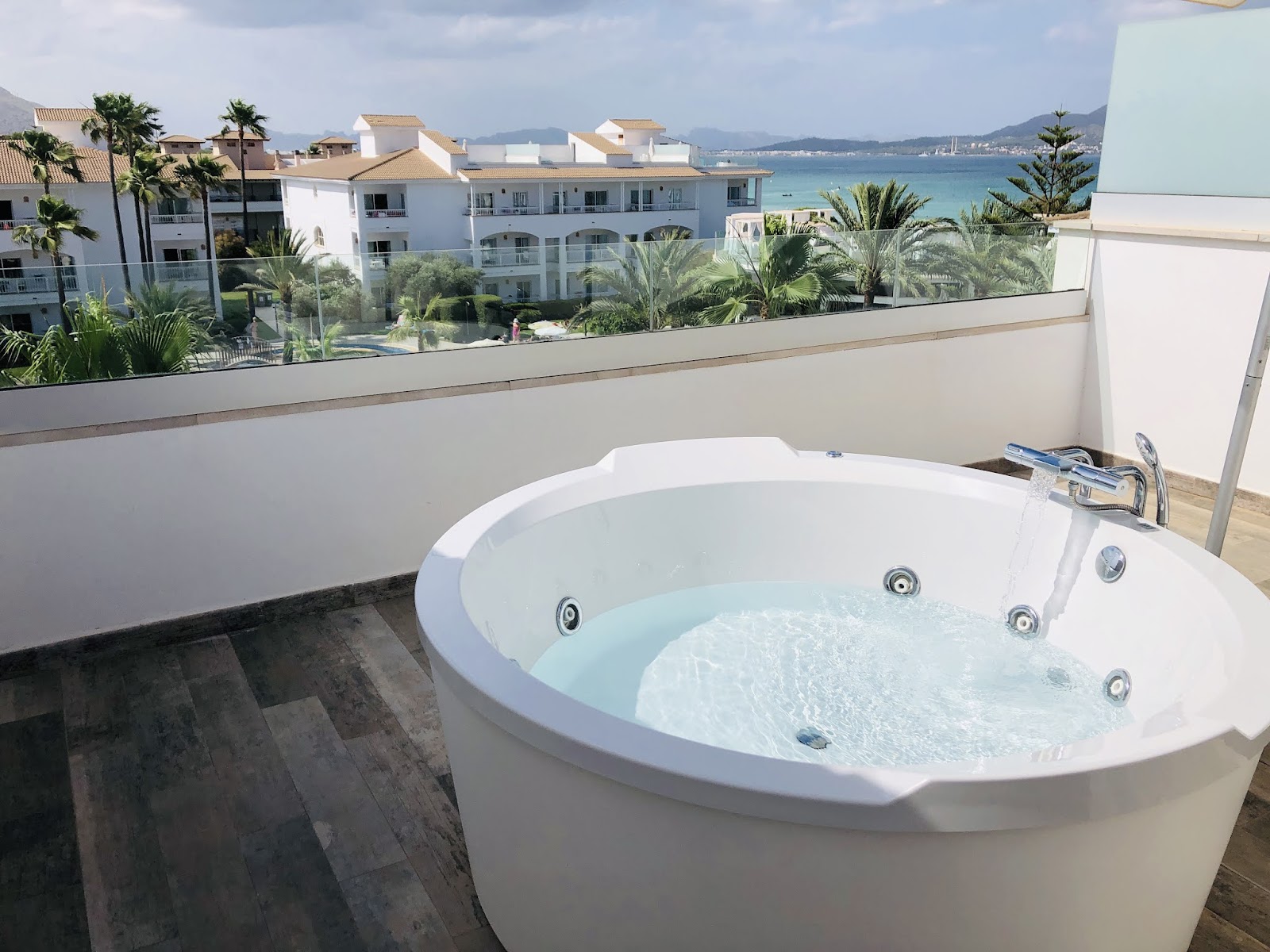 Jacuzzi on a private terrace with bay views, white resort buildings and palm trees visible beyond the wall.
