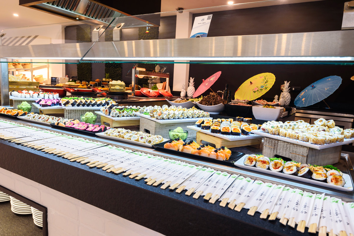 Sushi bar display at Playa Garden Selection Hotel & Spa with numerous rolls and sashimi arranged in trays, colorful parasols and pineapple decorations in background.