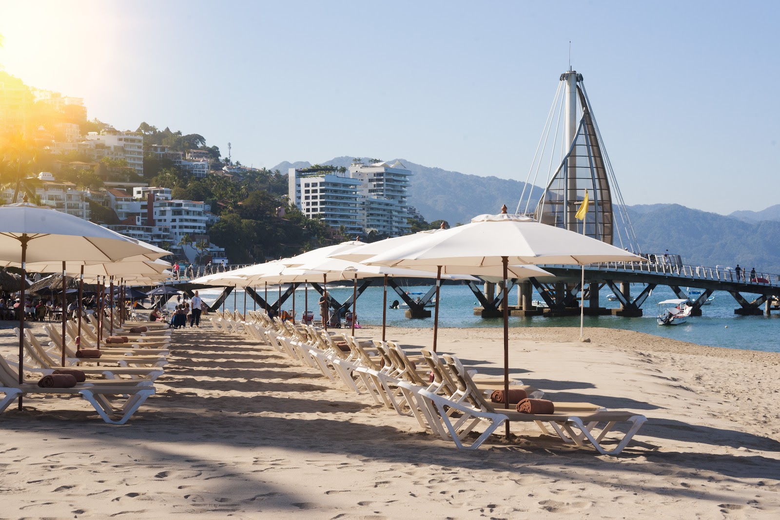 Beach lined with white lounge chairs and cream umbrellas, turquoise ocean waves, and high-rise resort buildings visible along the shoreline.