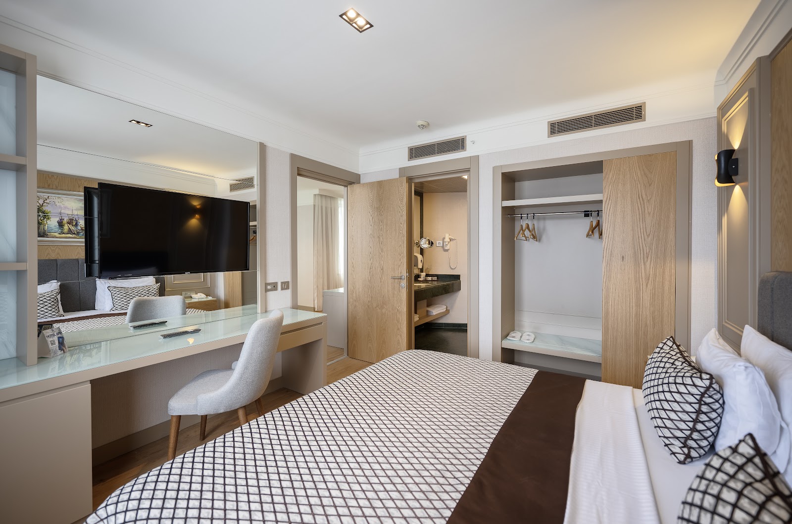 Spacious resort room with two beds, vanity desk with TV, seating area, and modern neutral décor with warm lighting.