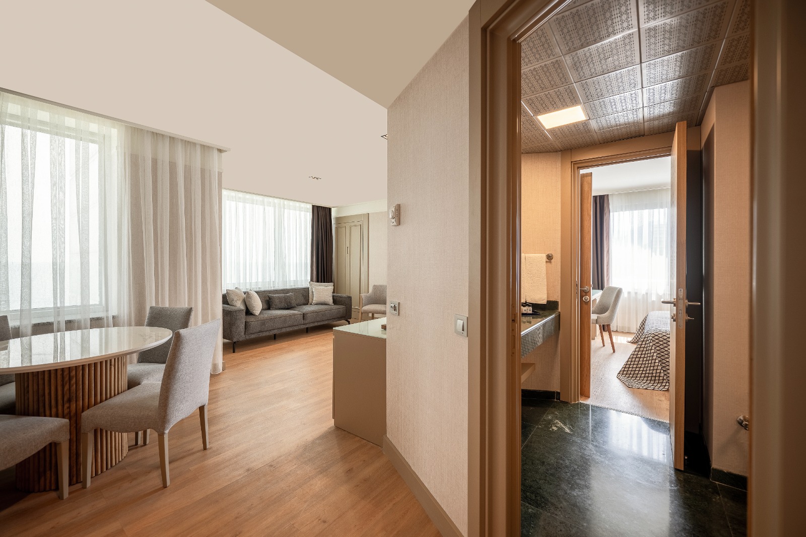 Modern suite with open layout showing dining area, living room with gray sofa, and hallway leading to bedroom at Porto Bello Hotel Resort & Spa.