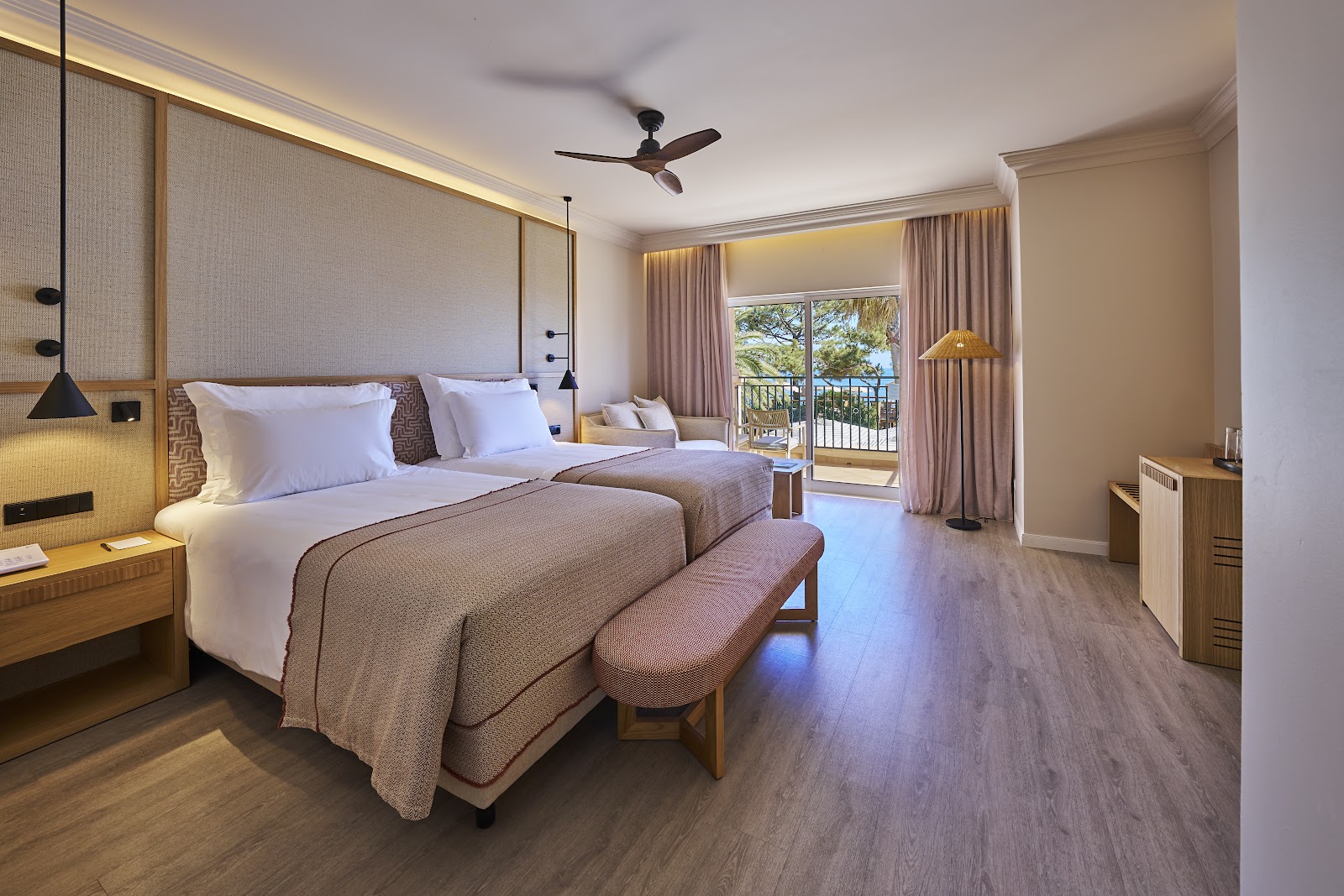 Spacious resort bedroom with king bed, seating area, and balcony overlooking ocean and greenery.