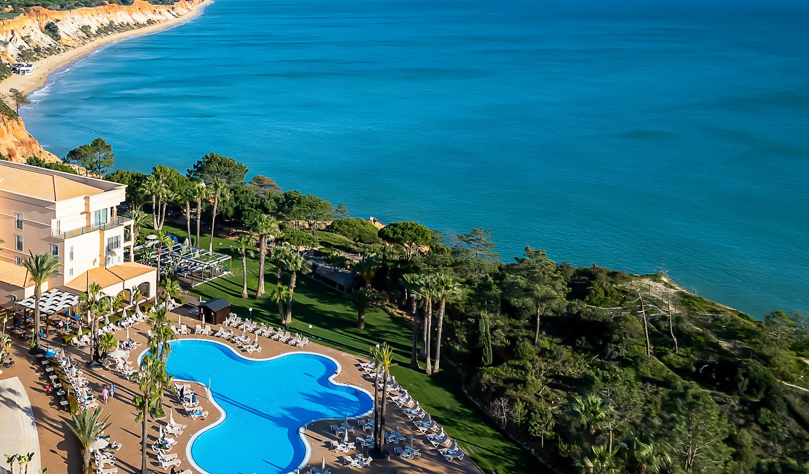 Resort pool and terraced grounds overlook turquoise bay waters and ochre cliffs along the Portuguese coast.