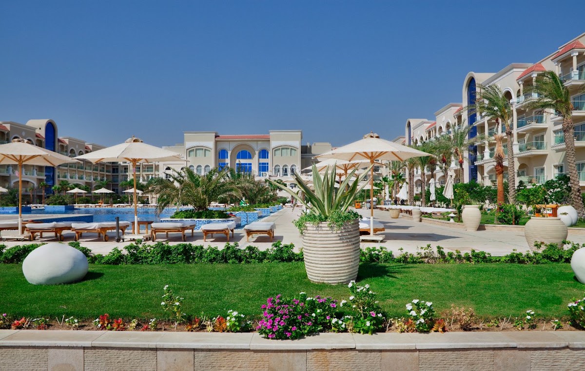Lawn and flower beds overlook the pool area and cream-colored buildings with blue accents at Premier Le Reve Hotel & Spa, with tan umbrellas and lounge chairs.