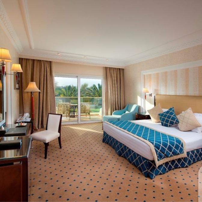 Spacious resort bedroom with blue patterned bedding, sitting area, and balcony overlooking tropical grounds at Premier Le Reve Hotel & Spa.