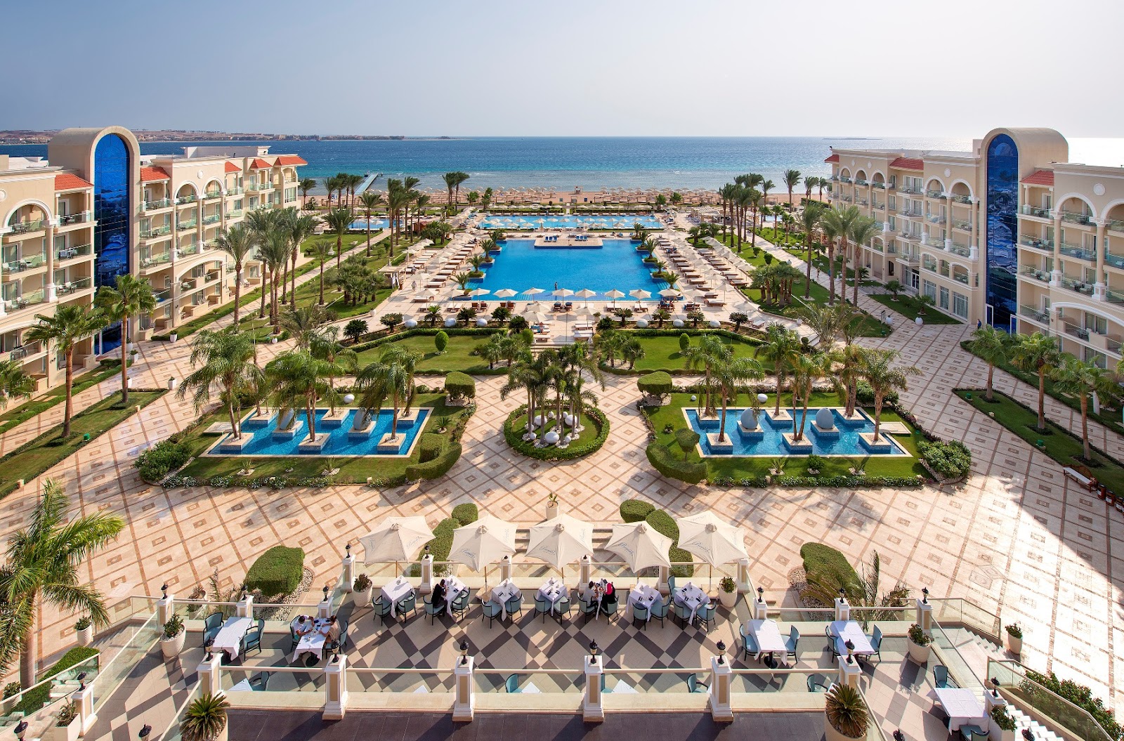 Aerial view of Premier Le Reve Hotel & Spa showing twin resort buildings flanking a central pool complex with lounge chairs, beach beyond, and Mediterranean Sea.
