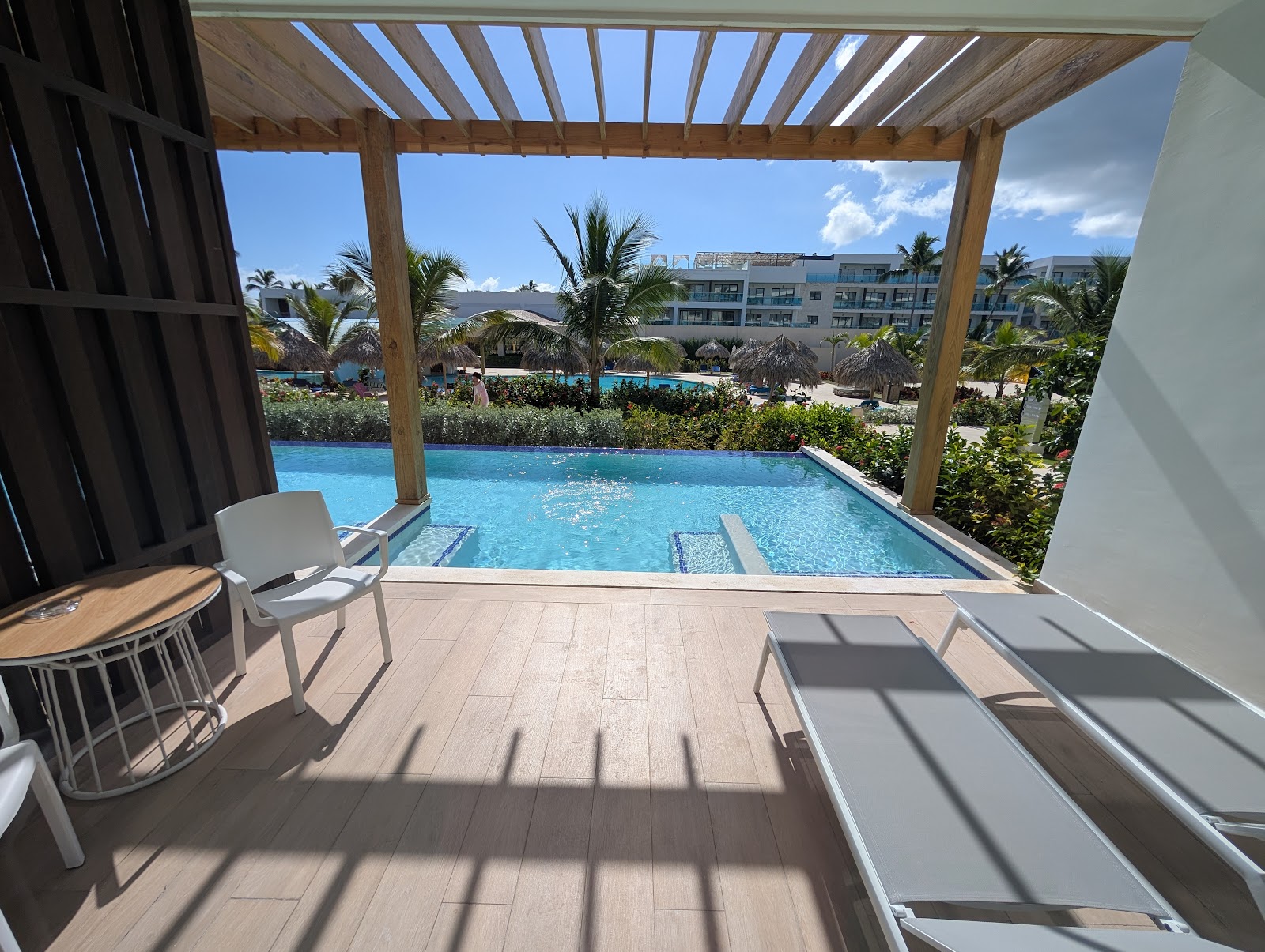 Private pool deck with lounge chairs under wooden pergola overlooking resort grounds, palm trees, and additional pools beyond.