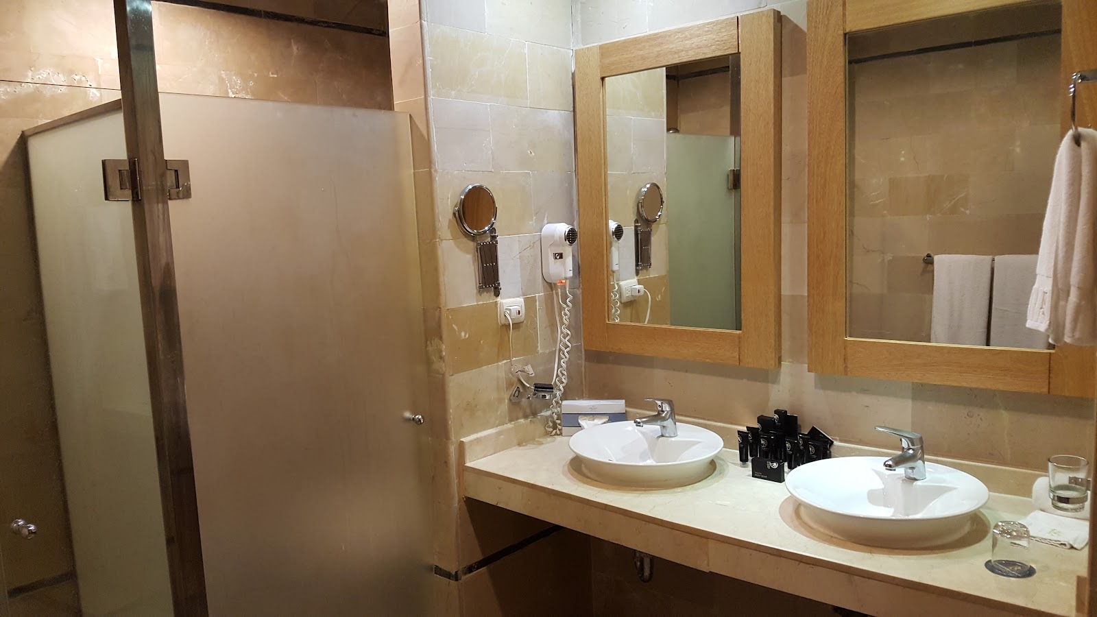 Resort bathroom with two round white sinks, wooden-framed mirrors, a glass shower enclosure, and amenity bottles on the counter.