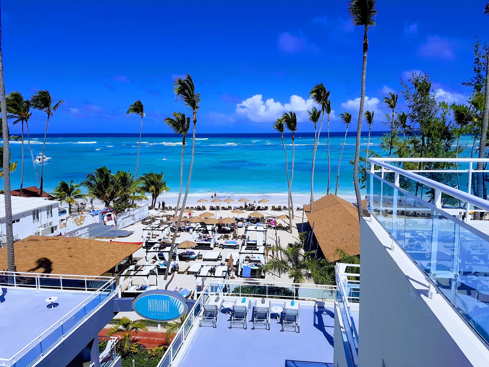 Beachfront view of Presidential Suites Punta Cana with turquoise ocean, palm trees, lounge chairs, and thatched umbrellas on white sand.