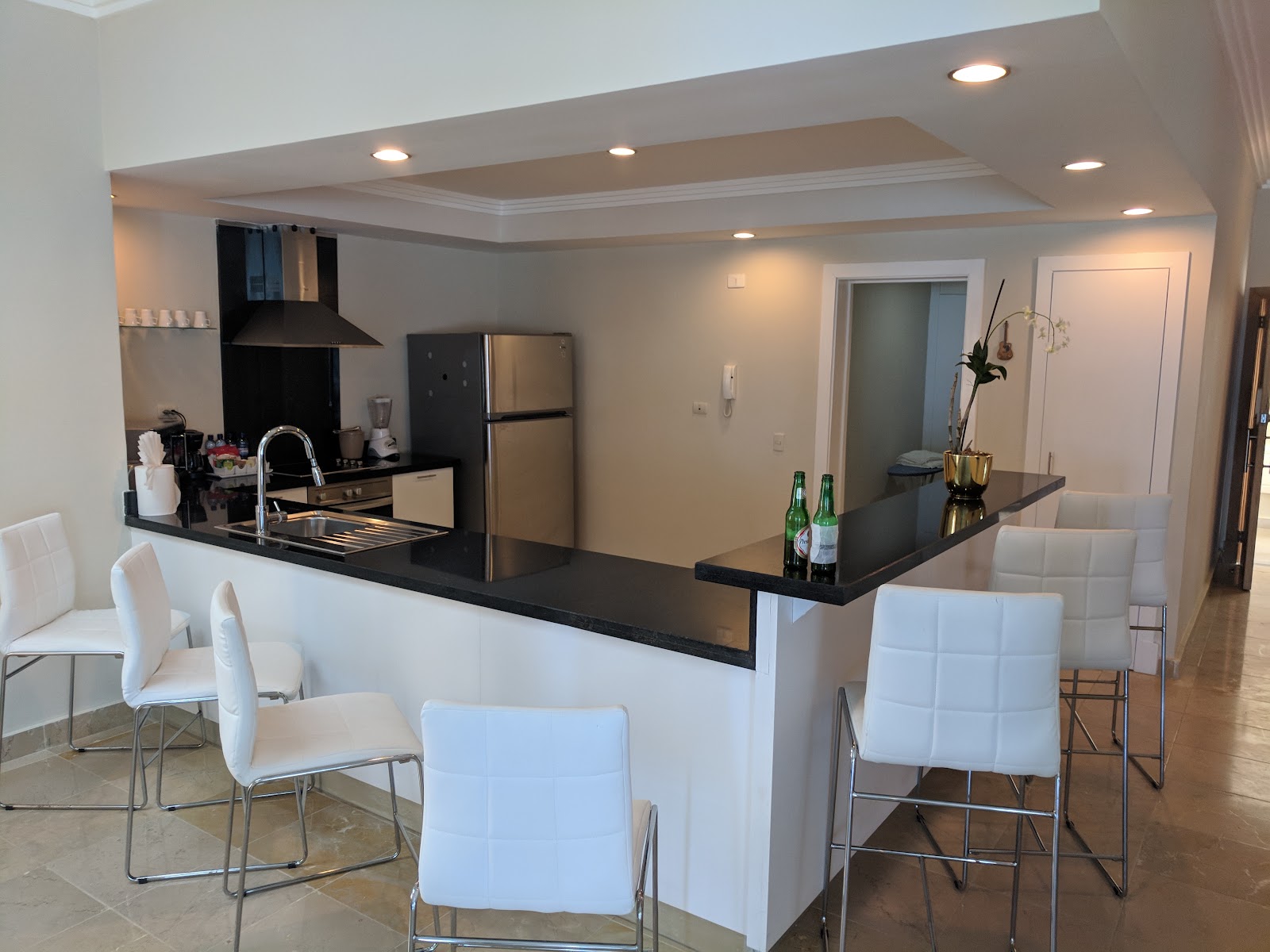 Kitchen and dining area with black countertop, stainless steel appliances, white bar stools, and recessed ceiling lights.