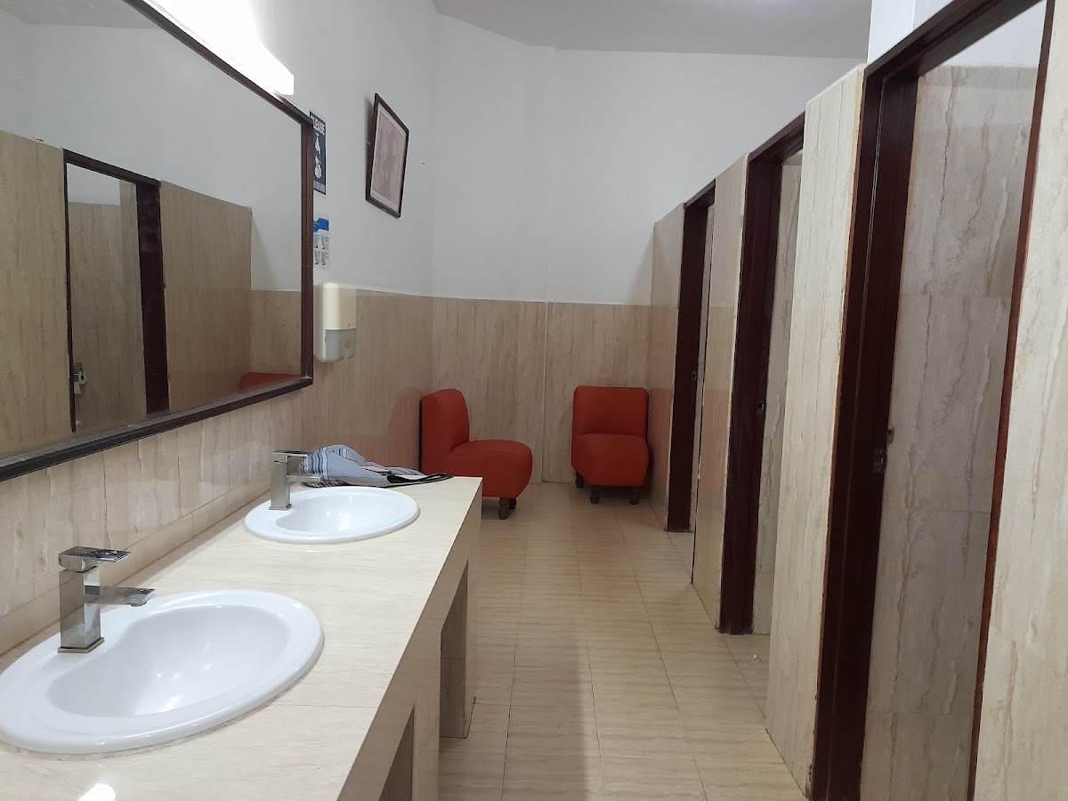 PrideInn Flamingo Beach Resort shared bathroom with two sinks, mirrors, red chairs, and multiple stall doors along wood-paneled walls.