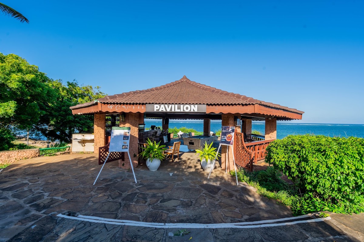 Beachfront pavilion with thatched roof and orange awning overlooks turquoise ocean waters under clear blue sky.