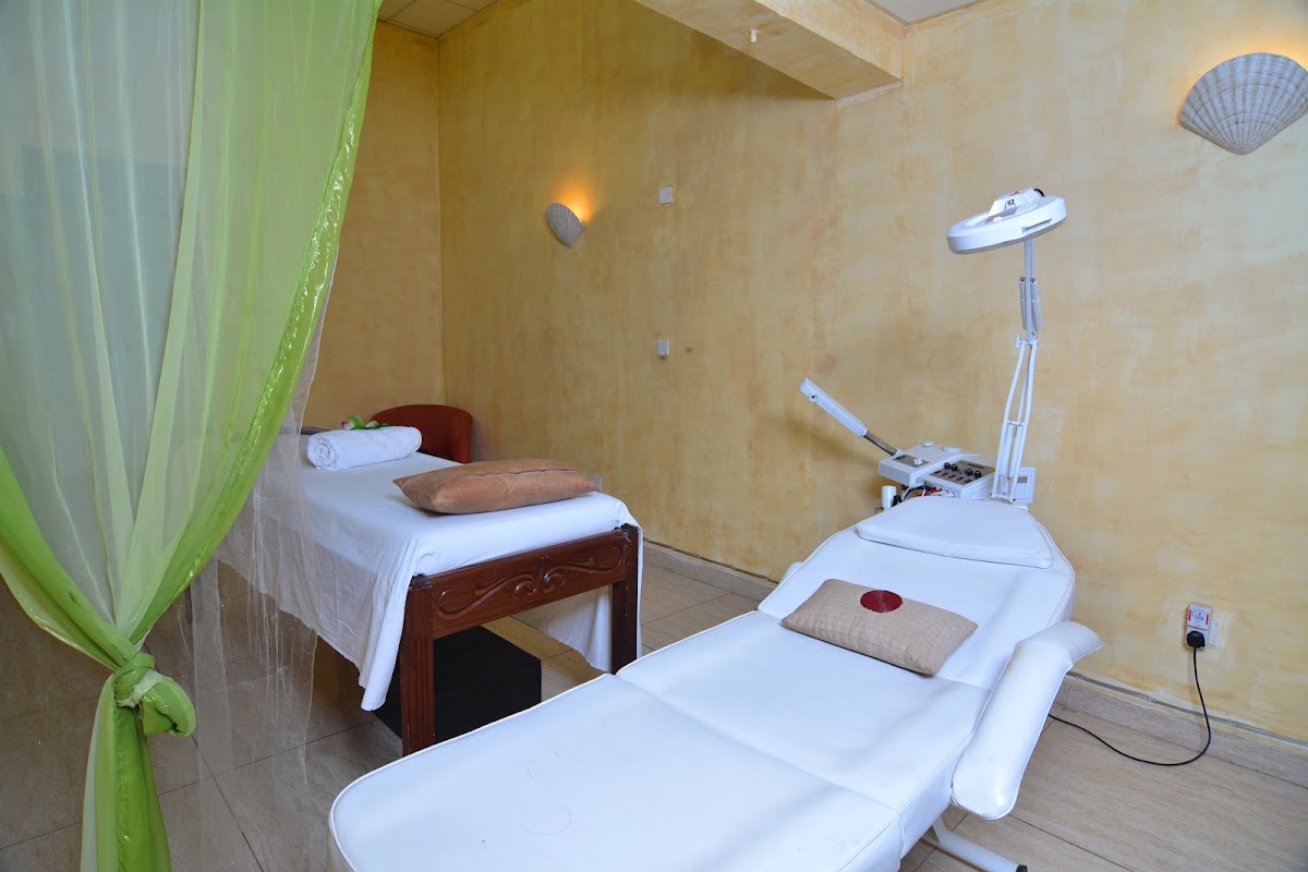 Spa treatment room with white massage bed in foreground, wooden bed with white linens in background, and green sheer curtain dividing the space.