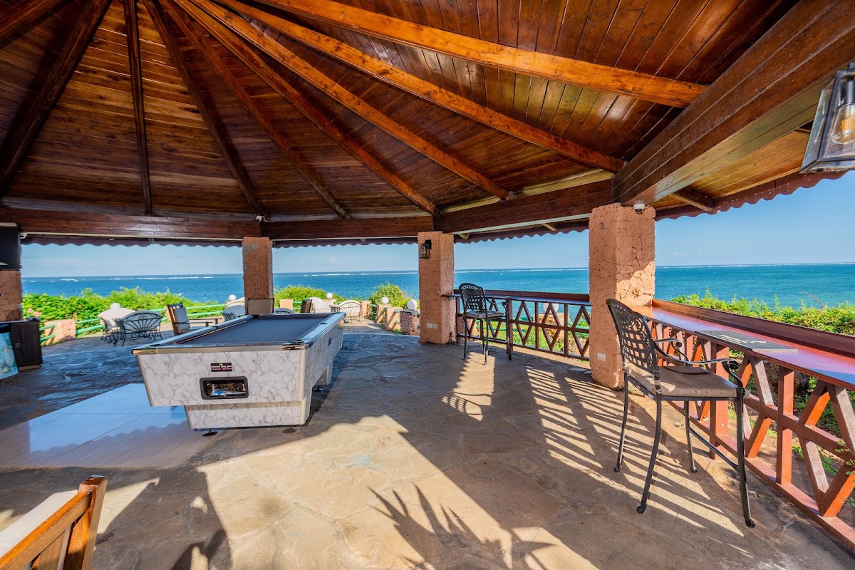 Open-air pavilion with wooden beamed ceiling overlooking the ocean, featuring a pool table, seating, and ocean views at PrideInn Flamingo Beach Resort & Spa.