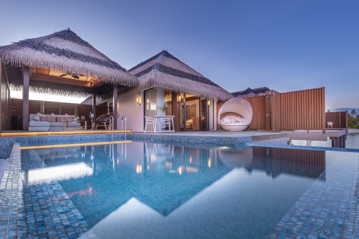 Overwater bungalows with thatched roofs and private pools at Pullman Maldives Maamutaa at dusk.