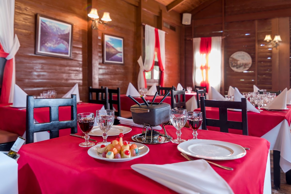 Dining room with bright pink tablecloths, place settings, and appetizer plates at wooden tables with black chairs under warm lighting.