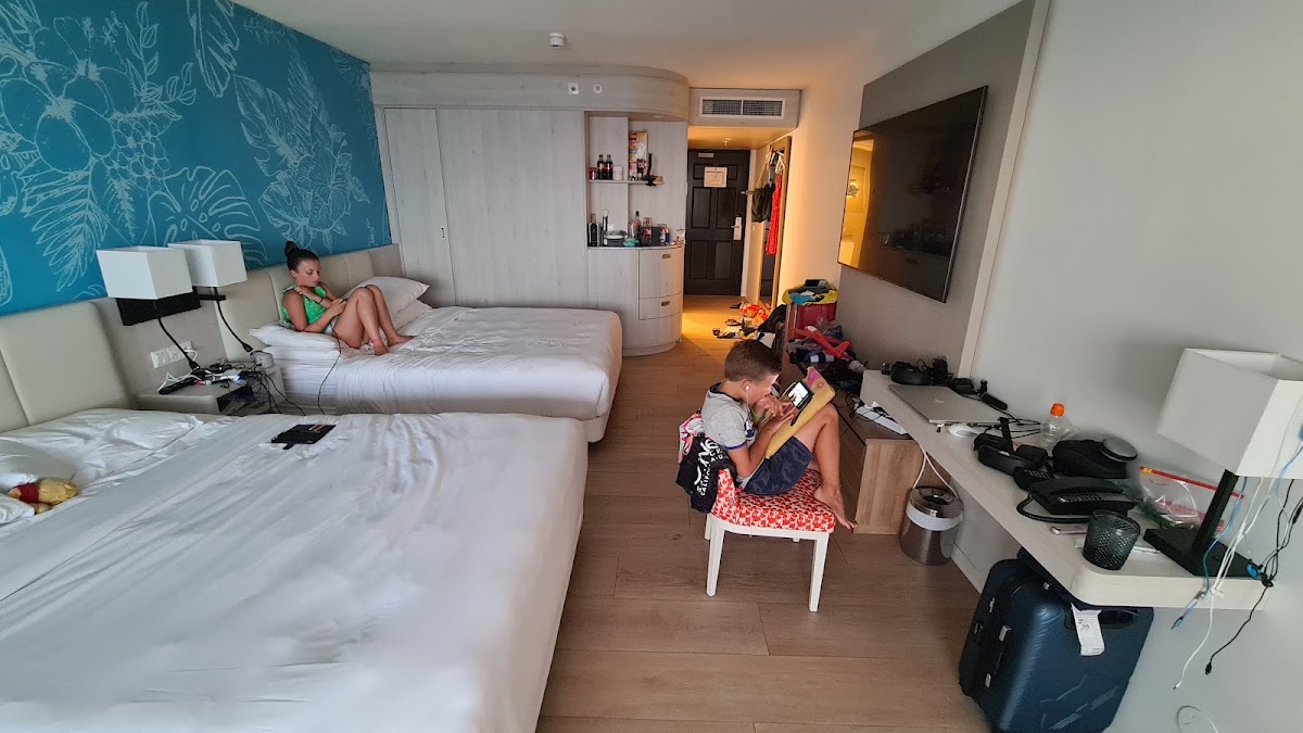 Family room with two beds, teal accent wall with floral design, and two children during their stay at The Pyrmont Curaçao.