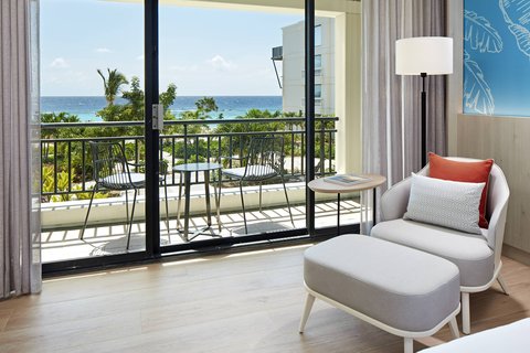 Guest room with gray chair and ocean view from balcony at The Pyrmont Curaçao.