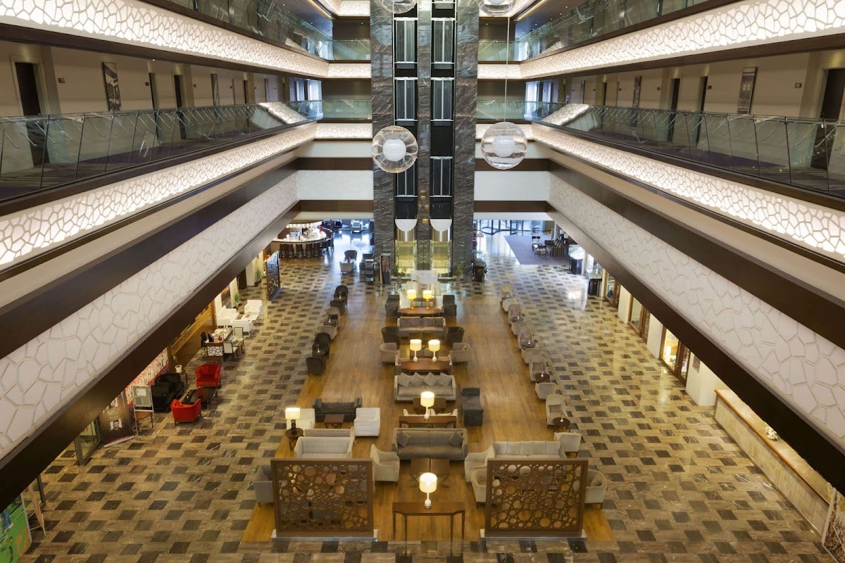 Multi-level atrium lobby with seating areas, geometric patterned floors, and illuminated ceiling at Ramada Plaza by Wyndham Antalya.