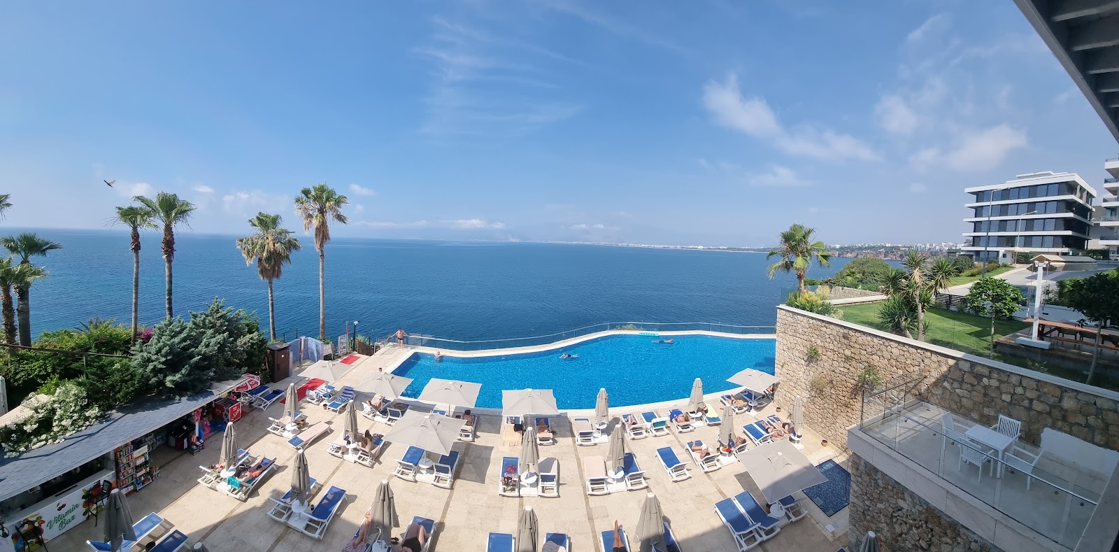 Curved swimming pool overlooking the Mediterranean Sea at Ramada Plaza by Wyndham Antalya, with loungers, umbrellas, and palm trees.
