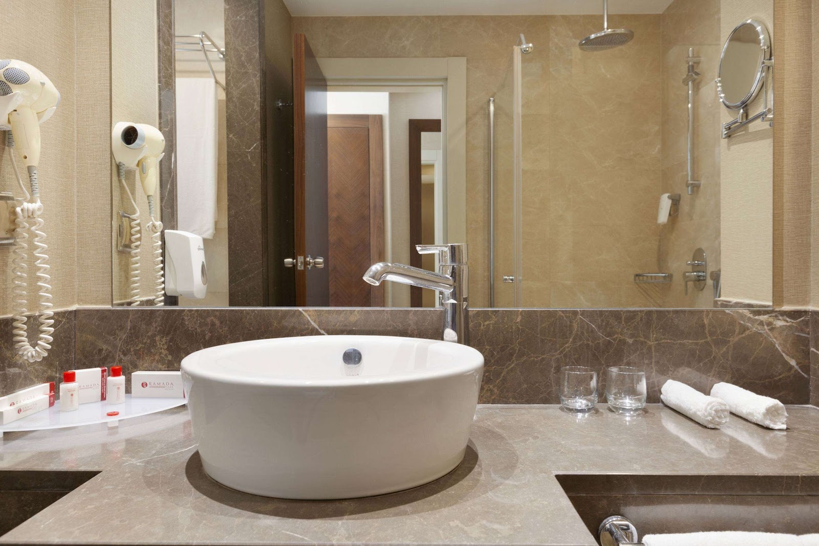 Bathroom with round white soaking tub on marble countertop, glass shower enclosure, and amenities on counter.