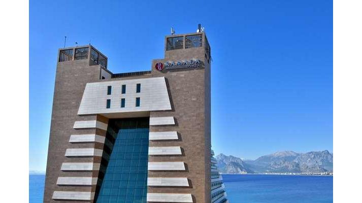 Ramada Plaza by Wyndham Antalya's distinctive tower with striped facade and blue-tinted glass entrance overlooks the Mediterranean Sea and coastal mountains.