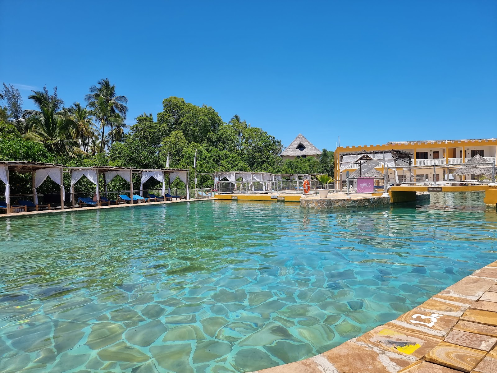 Blue pool with loungers and umbrellas overlooking turquoise lagoon waters and palm trees at Reef & Beach Resort.