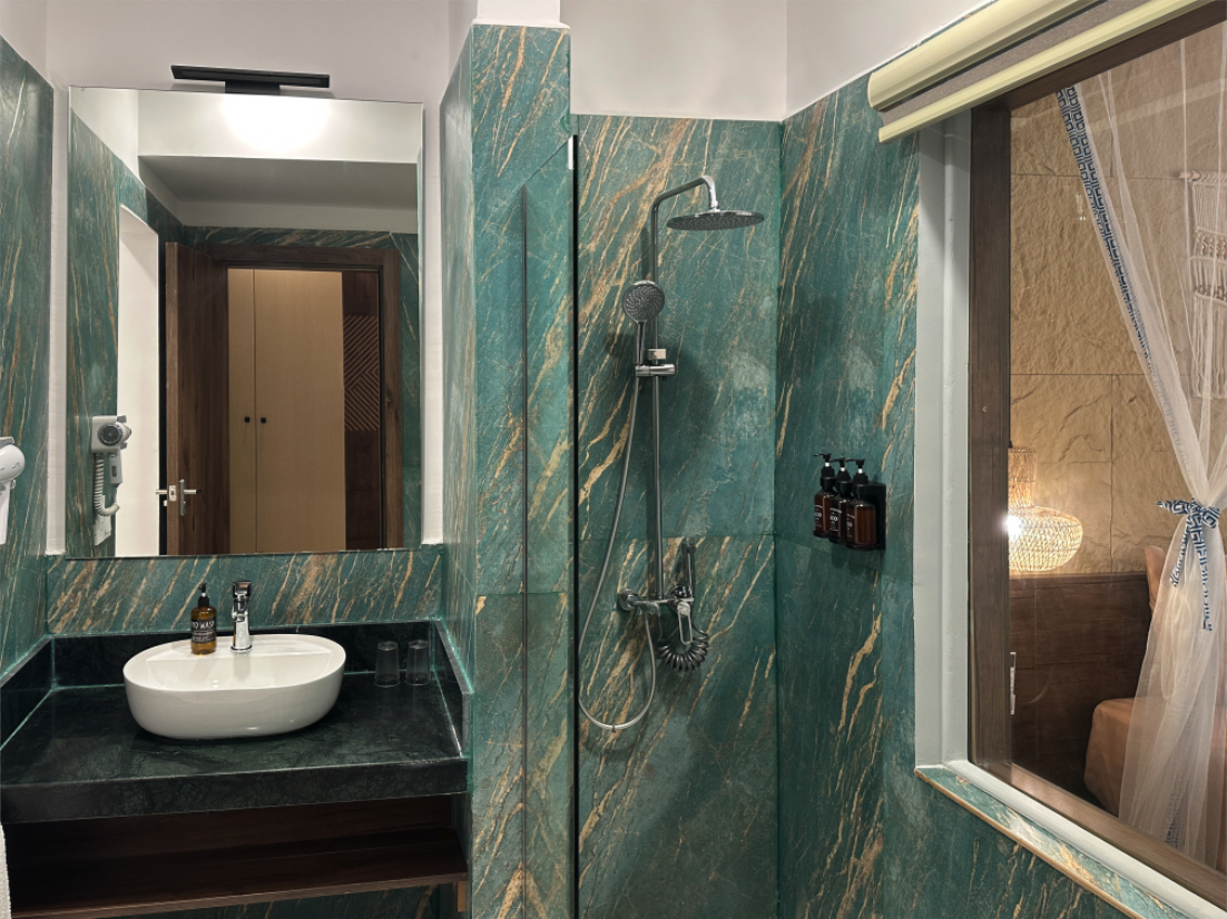 Bathroom with teal marble walls, round white sink, and walk-in shower with rainfall showerhead at Reef & Beach Resort.