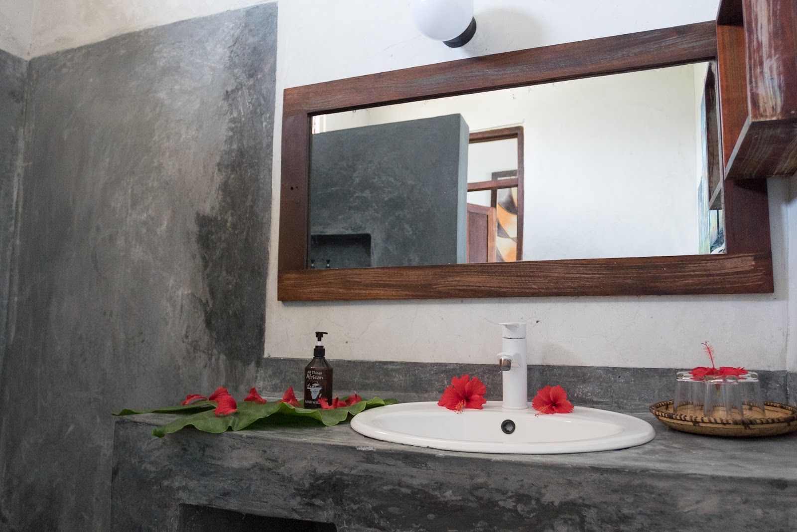 Bathroom sink with round white basin, dark concrete countertop, wood-framed mirror, and red flowers arranged on the counter.