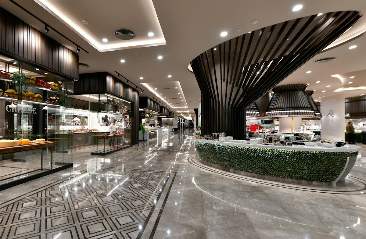 Modern indoor food court with black slatted architectural elements, multiple dining counters with glass displays, polished gray floor, and green plant accents.