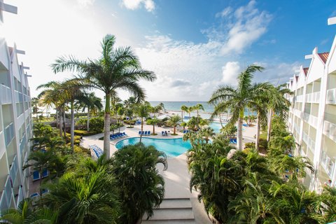 Renaissance Wind Creek Aruba Resort pool area with palm trees, white buildings, and ocean view under blue sky.