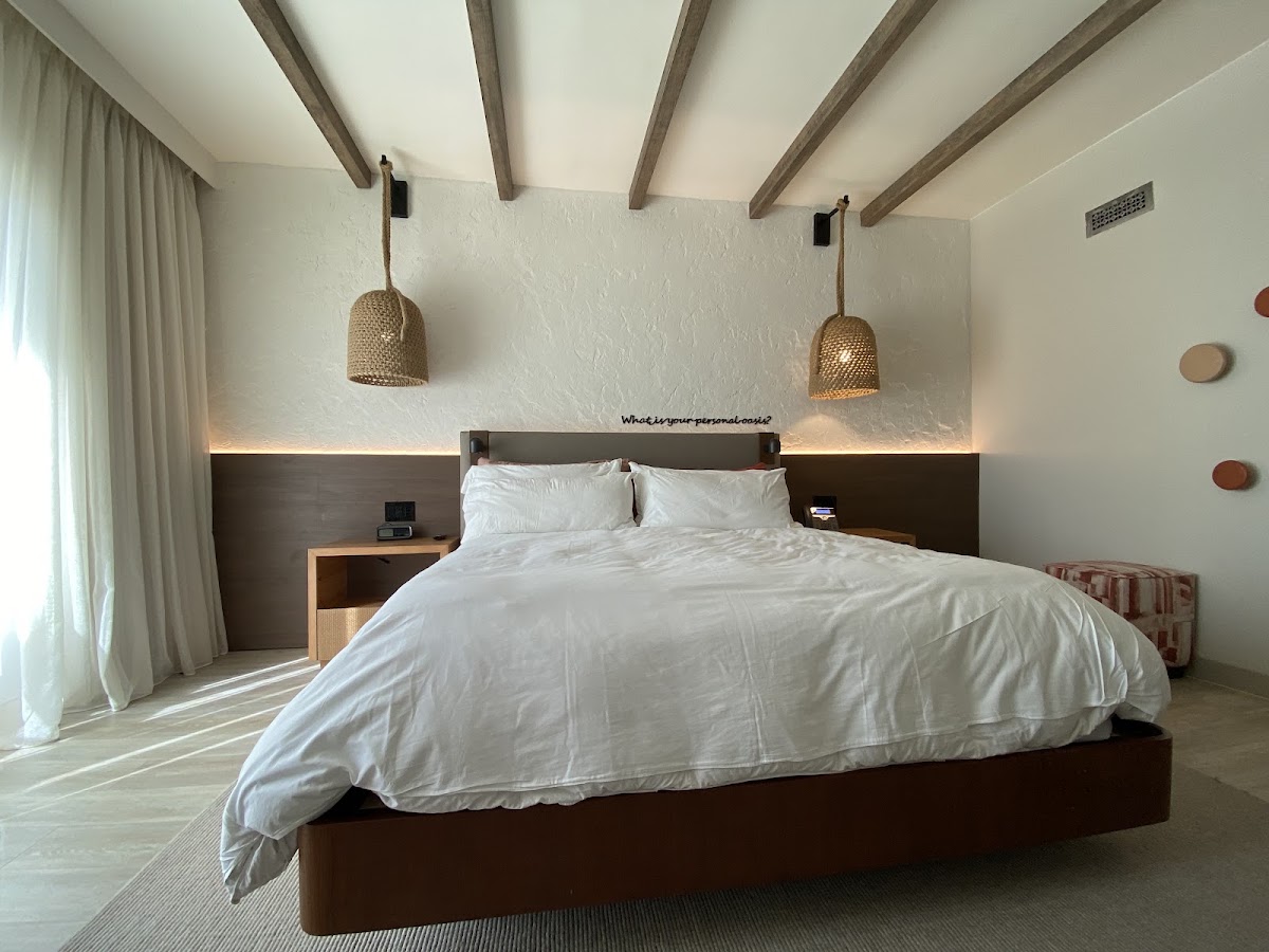 Modern bedroom with dark wood bed frame, white bedding, exposed beam ceiling, woven pendant lights, and floor-to-ceiling curtains.