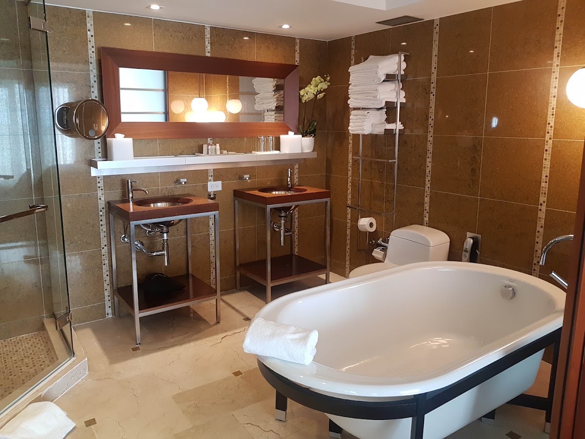 Bathroom with soaking tub, dual wooden vanities, walk-in shower, and stacked white towels on wall rack.